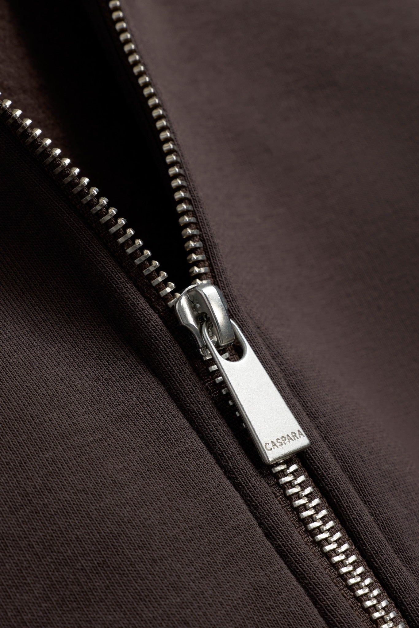 Close-up of the engraved silver zipper pull on an espresso brown CASPARA zip hoodie.